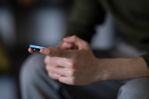 Close-up of a man's hands holding and using a smartphone while sitting on a sofa at home