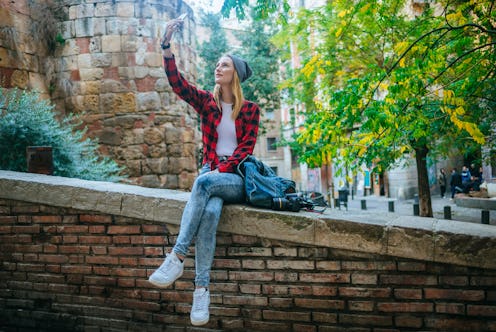 Young woman taking a selfie with a smart phone, sitting on the outside.