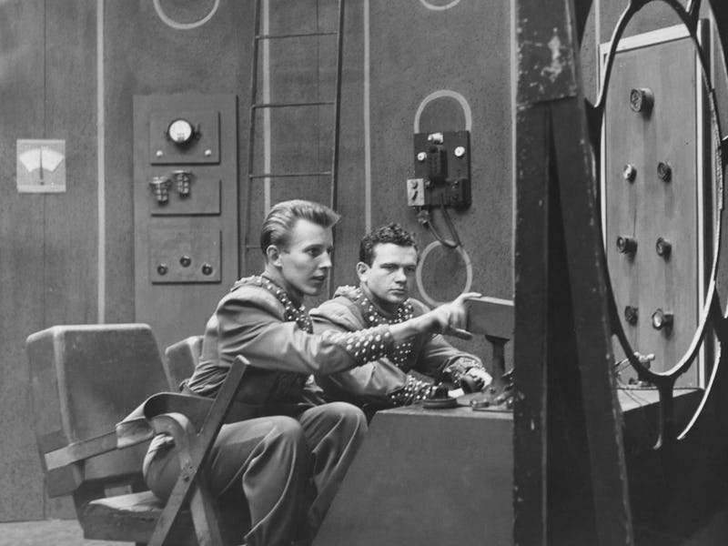 American actor Jan Merlin and American actor Frankie Thomas, both in costume, sit before a control p...