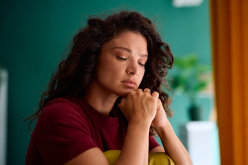 Sad woman in her 30s sitting alone at home, overwhelmed by feelings of loneliness and depression, re...