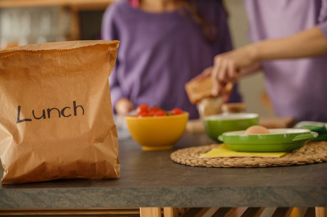 Selective focus of a brown paper bag with a word ''lunch'' on it in the focus in the foreground and ...