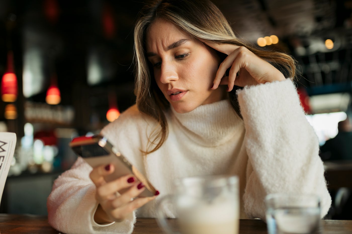 Worried young woman is reading bad news on her smartphone while sitting in a cafe