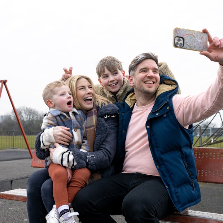 A wide shot of a mother and father sitting down on a bench with their children at a public park in D...