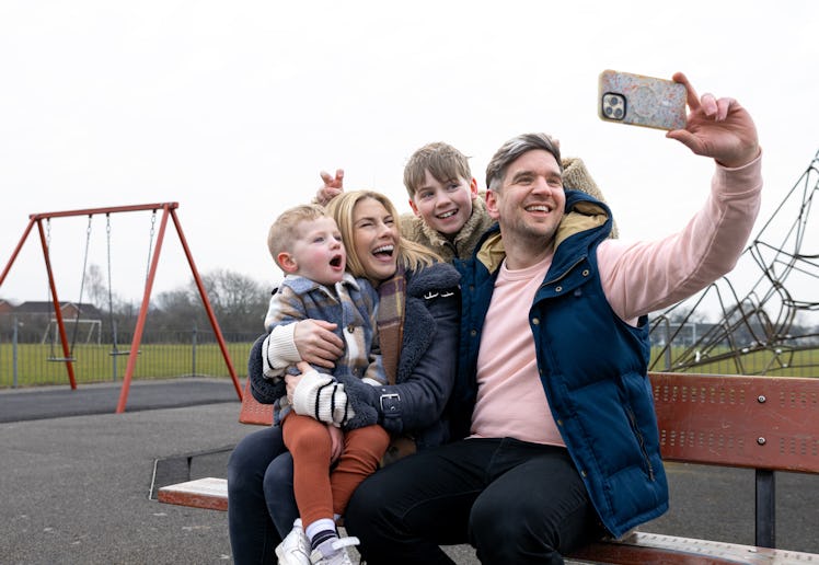 A wide shot of a mother and father sitting down on a bench with their children at a public park in D...