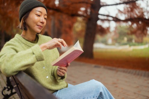 A 39 year old Korean woman wearing a green knit sweater and black beanie reads a book while sitting ...