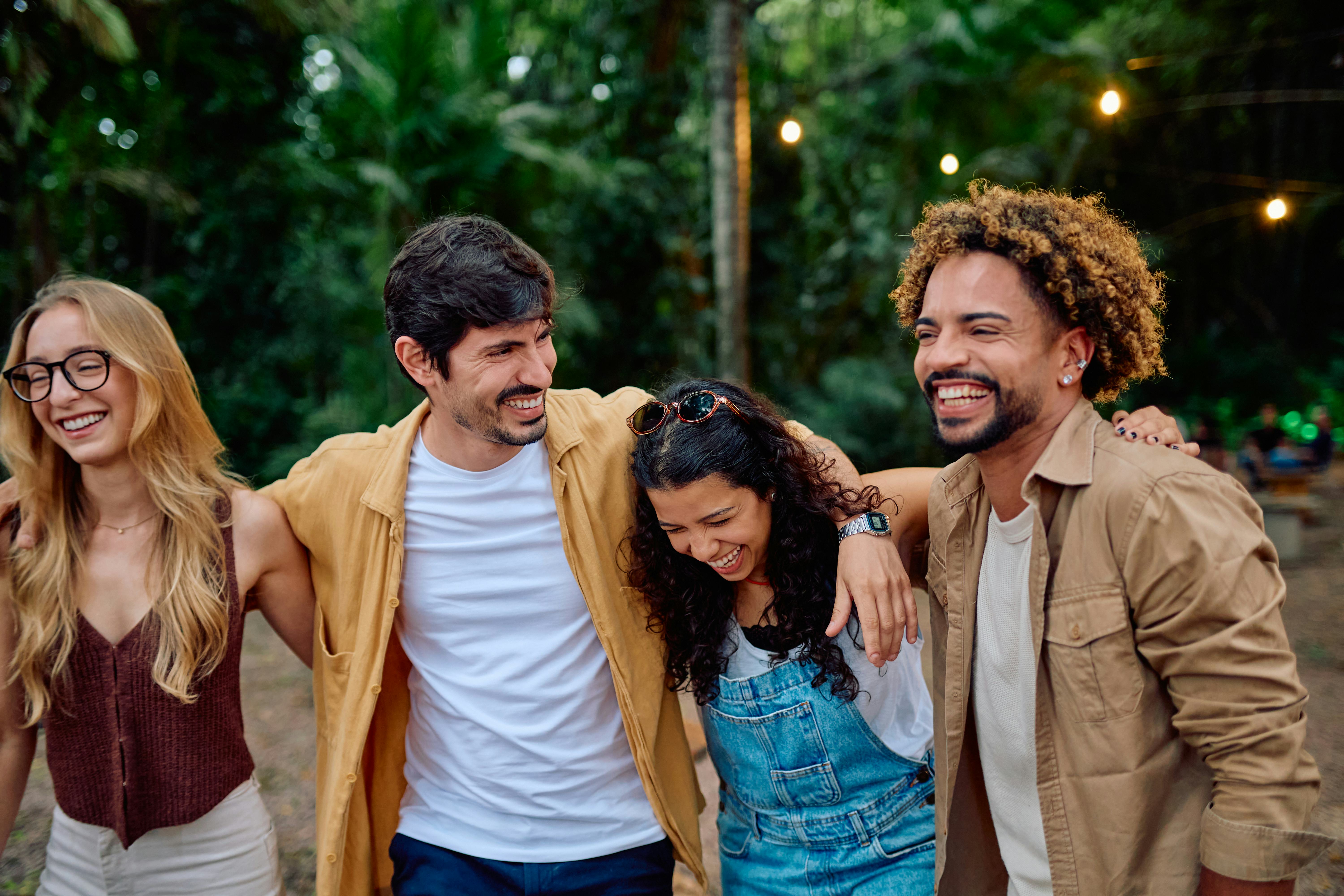 Happy four friends smiling, walking, and embracing outdoors. Enjoying friendship and having fun in n...