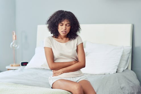 Shot of a young woman suffering from stomach cramps in her bedroom