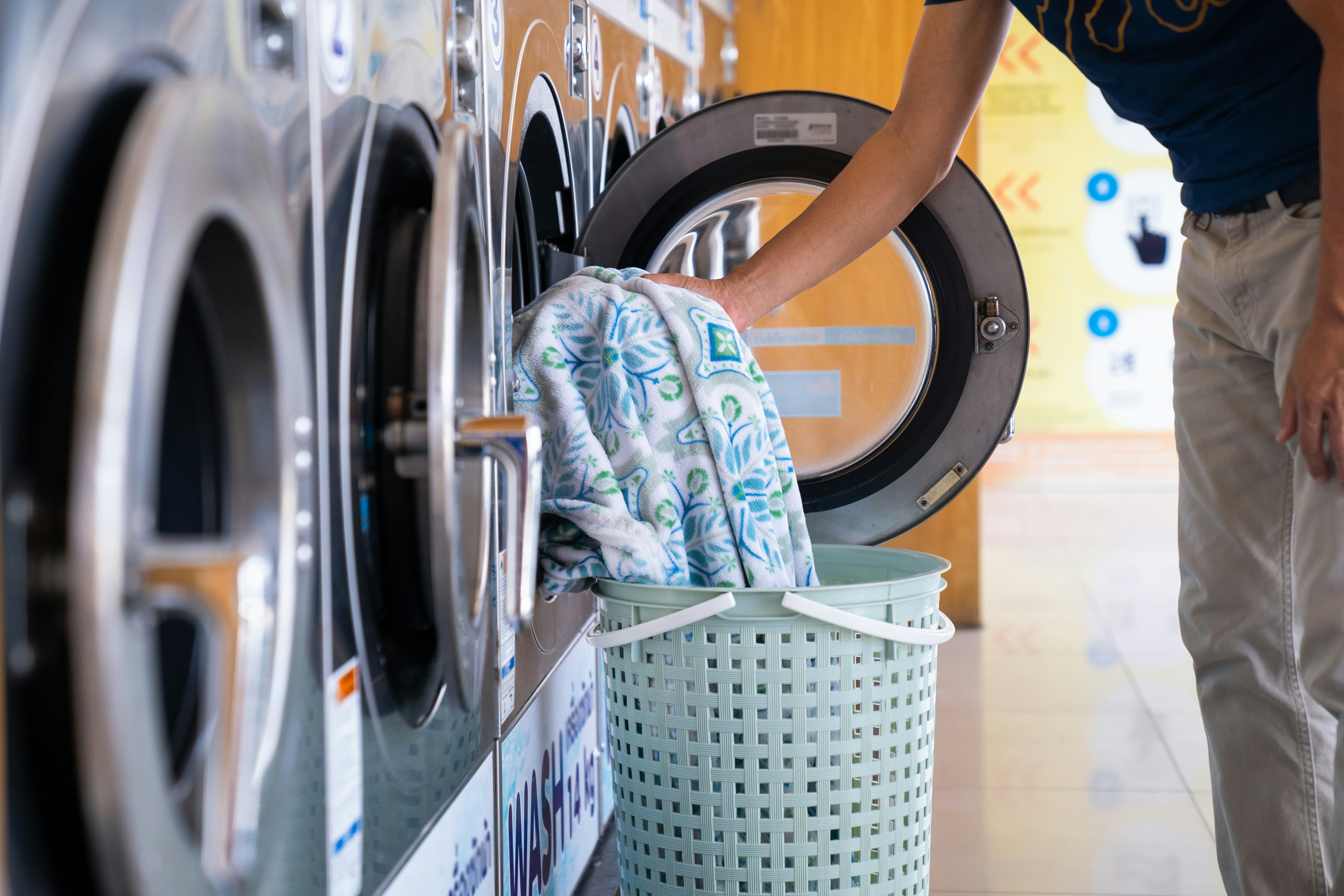 Man loading clothes into washing machine in laundromat.