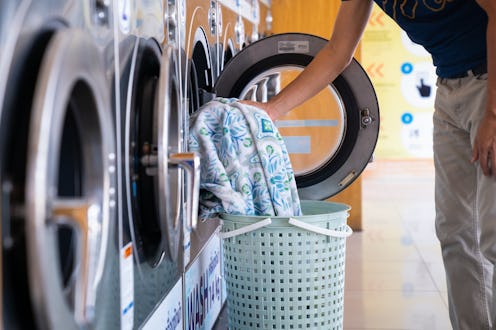 Man loading clothes into washing machine in laundromat.