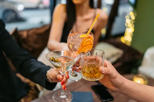 Group of three friends having a celebratory toast with cocktails and whiskey in a bar at night. Clos...
