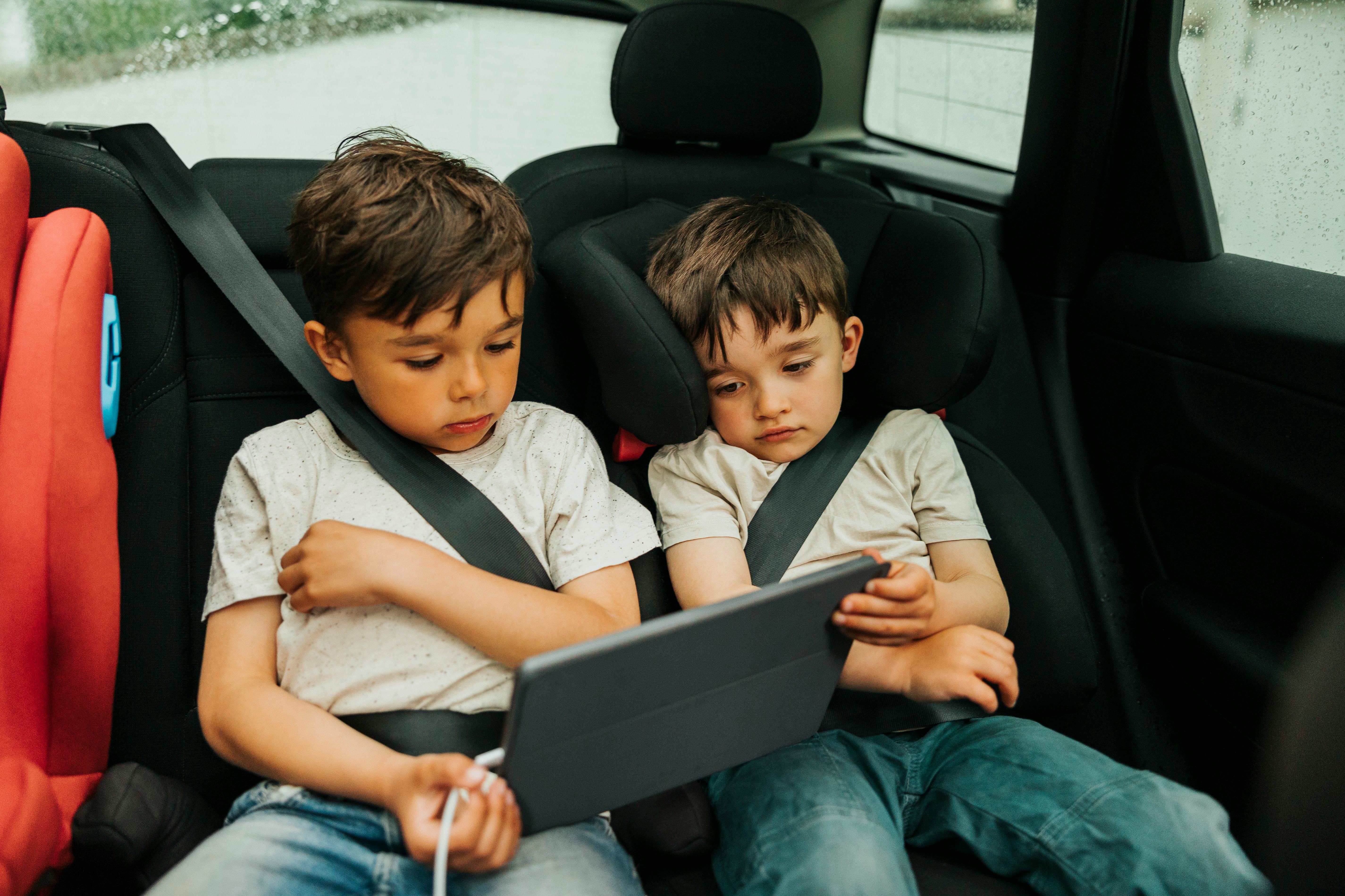 Two boys watch an iPad in the back of a car.