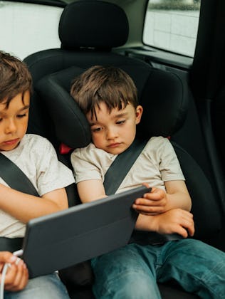 Two boys watch an iPad in the back of a car.