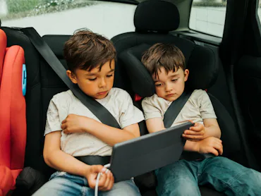 Two boys watch an iPad in the back of a car.