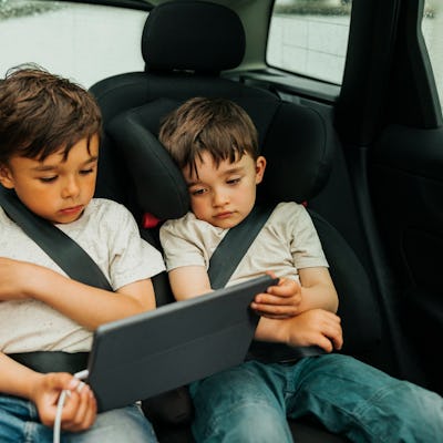 Two boys watch an iPad in the back of a car.
