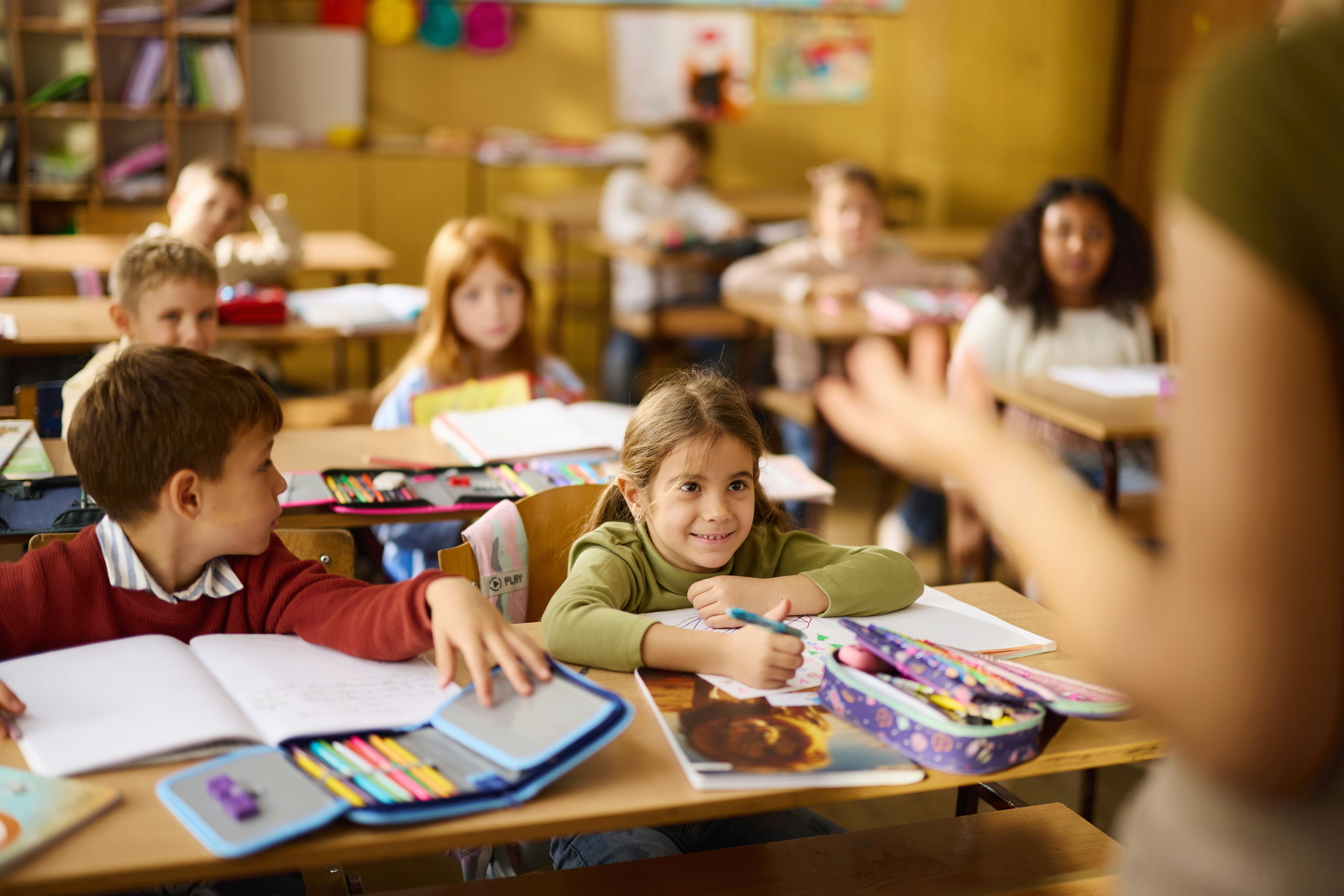 Large group of students paying attention on a class at elementary school. Focus is on happy girl.
