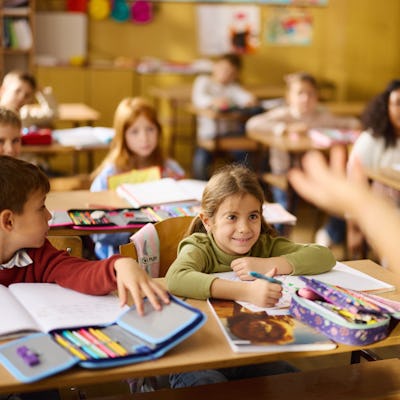 Large group of students paying attention on a class at elementary school. Focus is on happy girl.