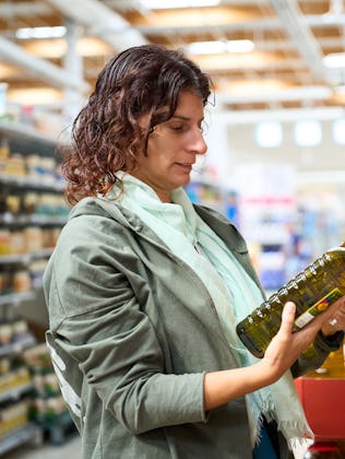 Woman in a grocery comparing prices of different olive oil bottles, facing economic financial crisis...
