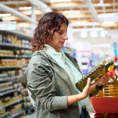 Woman in a grocery comparing prices of different olive oil bottles, facing economic financial crisis and inflation