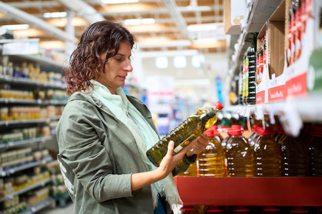 Woman in a grocery comparing prices of different olive oil bottles, facing economic financial crisis...