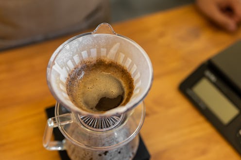Coffee brewing process with a pour-over dripper on a wooden table. Dark coffee grounds are visible i...