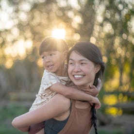 A boy holds on to his mother while riding piggy back. They are both smiling.