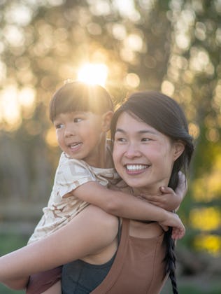 A boy holds on to his mother while riding piggy back. They are both smiling.
