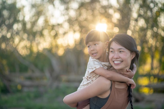 A boy holds on to his mother while riding piggy back. They are both smiling.