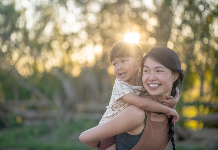 A boy holds on to his mother while riding piggy back. They are both smiling.