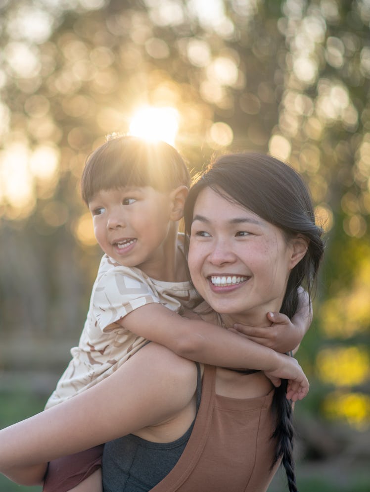 A boy holds on to his mother while riding piggy back. They are both smiling.