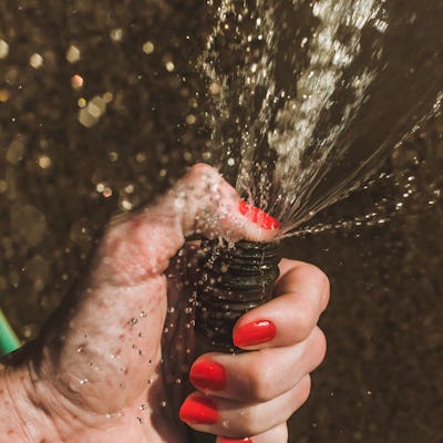 Closeup of water hose squirting water. Woman holding hose, woman with red nail polish, red nails, red fingernails closeup on hand gripping hose. Summer fun conceptual image for sexual issues, orgasm, and penis themes.