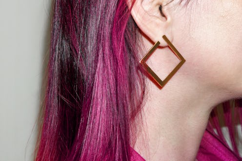 Stylish person showcases bold square earrings with vibrant pink hair in a close-up portrait taken in...
