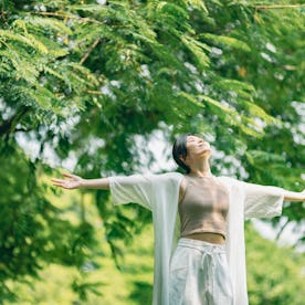 A woman stands in a park with her arms wide open to the sky.