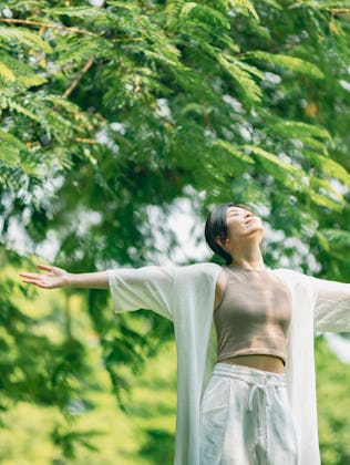 A woman stands in a park with her arms wide open to the sky.