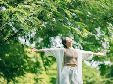 A woman stands in a park with her arms wide open to the sky.