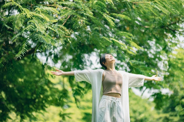 A woman stands in a park with her arms wide open to the sky.