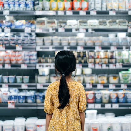 Rear view of Asian girl standing in front of a shelf full of fresh dairy products in the dairy aisle...