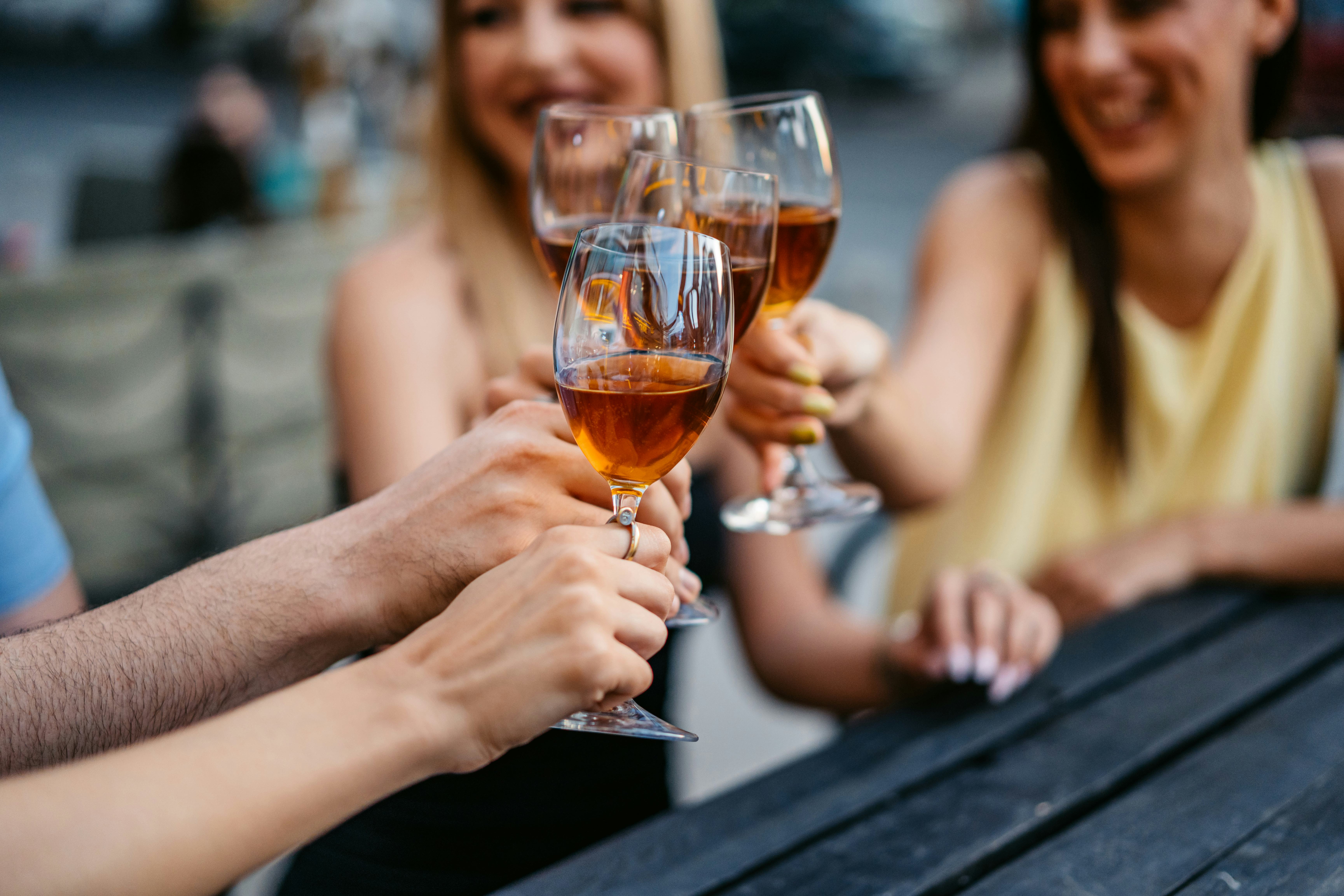 A group of four friends cheering with white wine in a bar outdoors. Close-up.