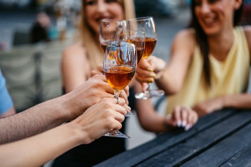A group of four friends cheering with white wine in a bar outdoors. Close-up.