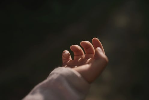 Tender little hand of child in dark key. Fingers close-up. Woman's happiness. Symbolic hand helping ...