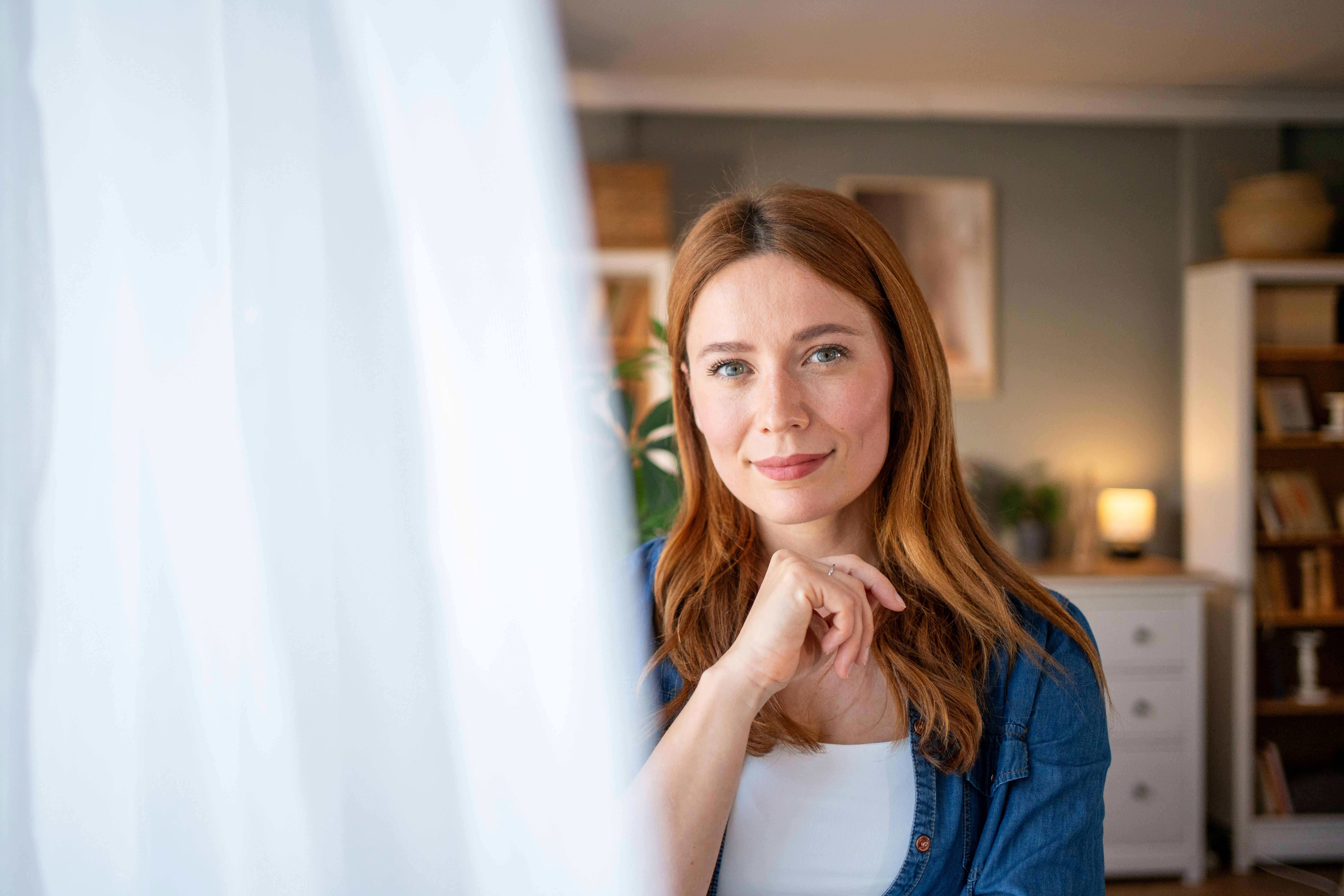 Portrait of a beautiful smiling mid adult woman with long red hair, wearing casual clothes, posing a...