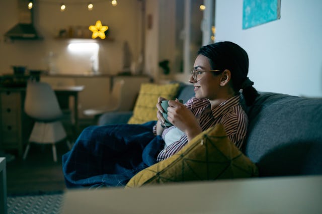 Young Caucasian woman drinking tea and watching tv during the relaxing evening at home.