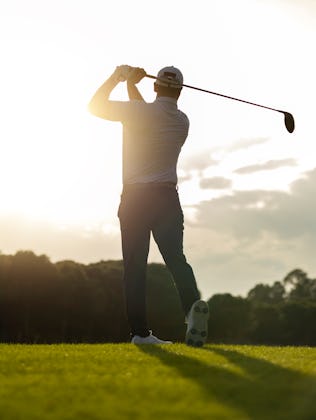 Silhouette of a golfer preparing to swing at sunrise on a bright fairway.