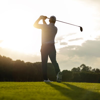Silhouette of a golfer preparing to swing at sunrise on a bright fairway.