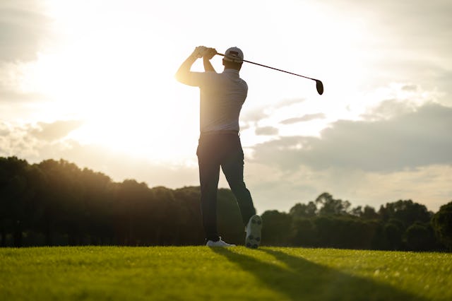 Silhouette of a golfer preparing to swing at sunrise on a bright fairway.
