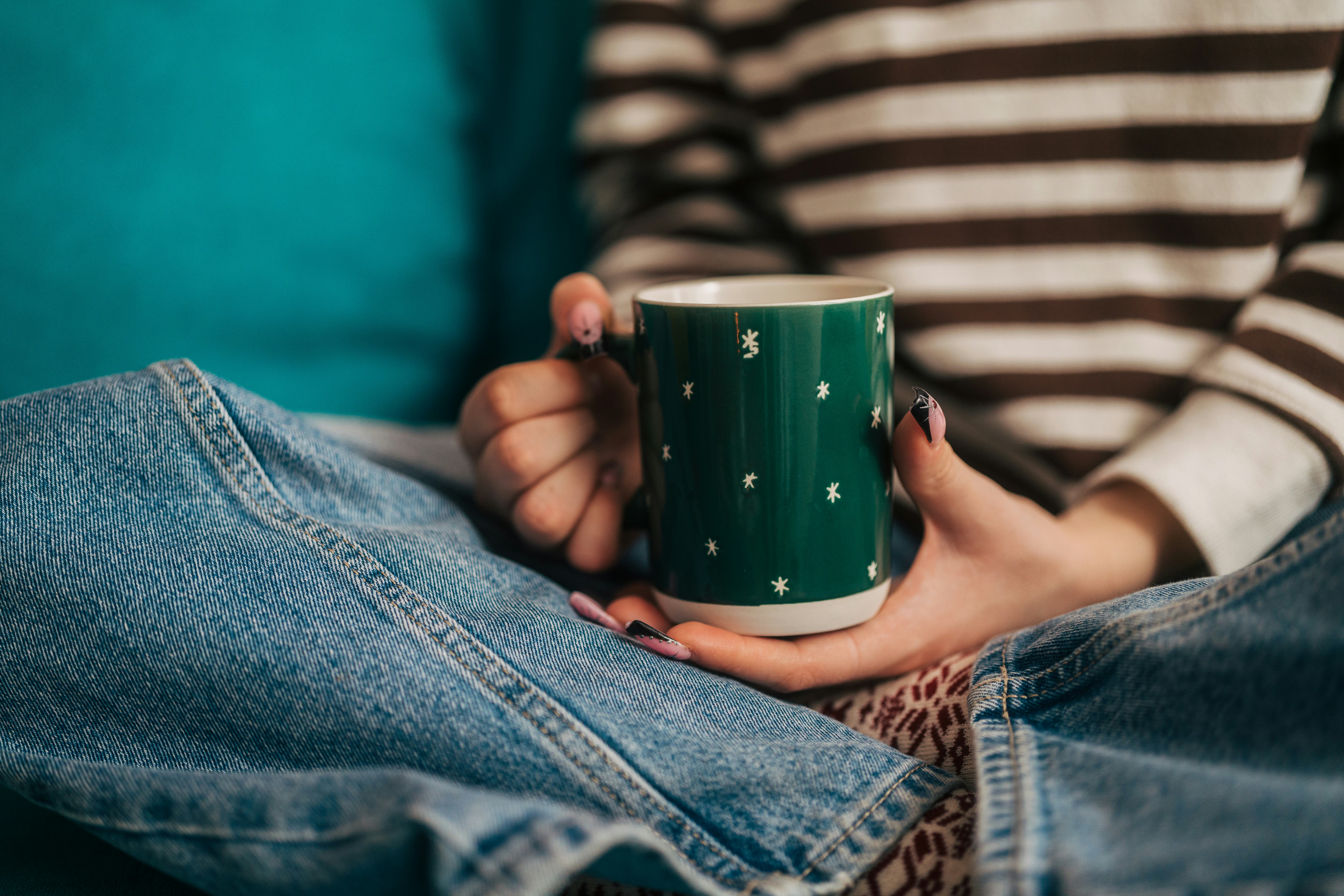 Young woman in a cozy sweater holding a warm mug, relaxing at home during winter, enjoying a peacefu...