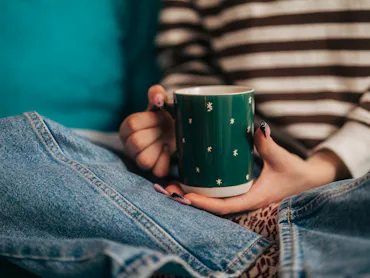 Young woman in a cozy sweater holding a warm mug, relaxing at home during winter, enjoying a peacefu...