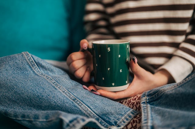 Young woman in a cozy sweater holding a warm mug, relaxing at home during winter, enjoying a peacefu...