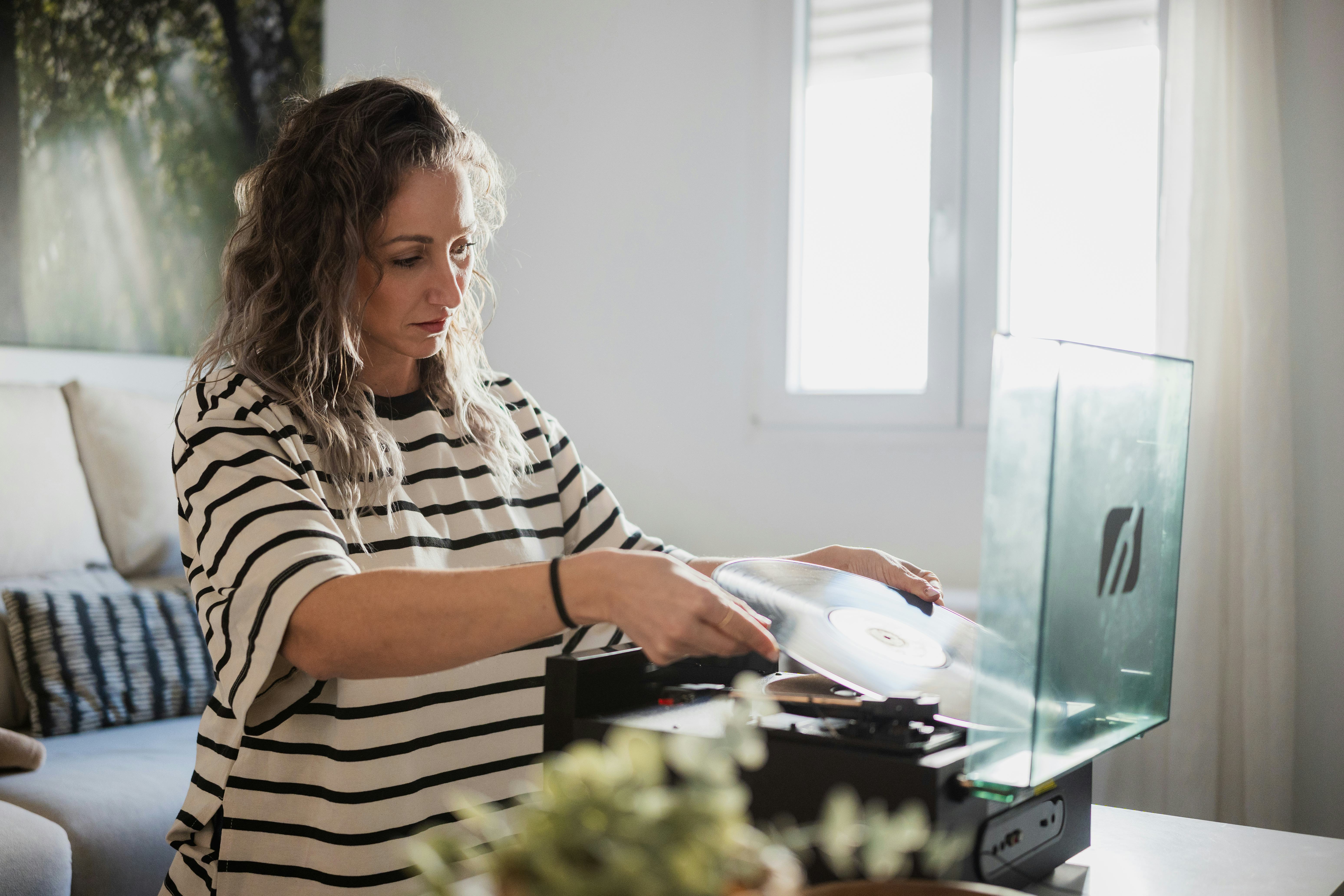 Woman carefully placing a vinyl record on a turntable, ready to enjoy music in her living room