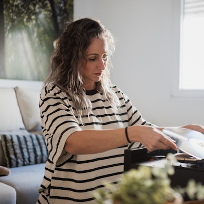 Woman carefully placing a vinyl record on a turntable, ready to enjoy music in her living room