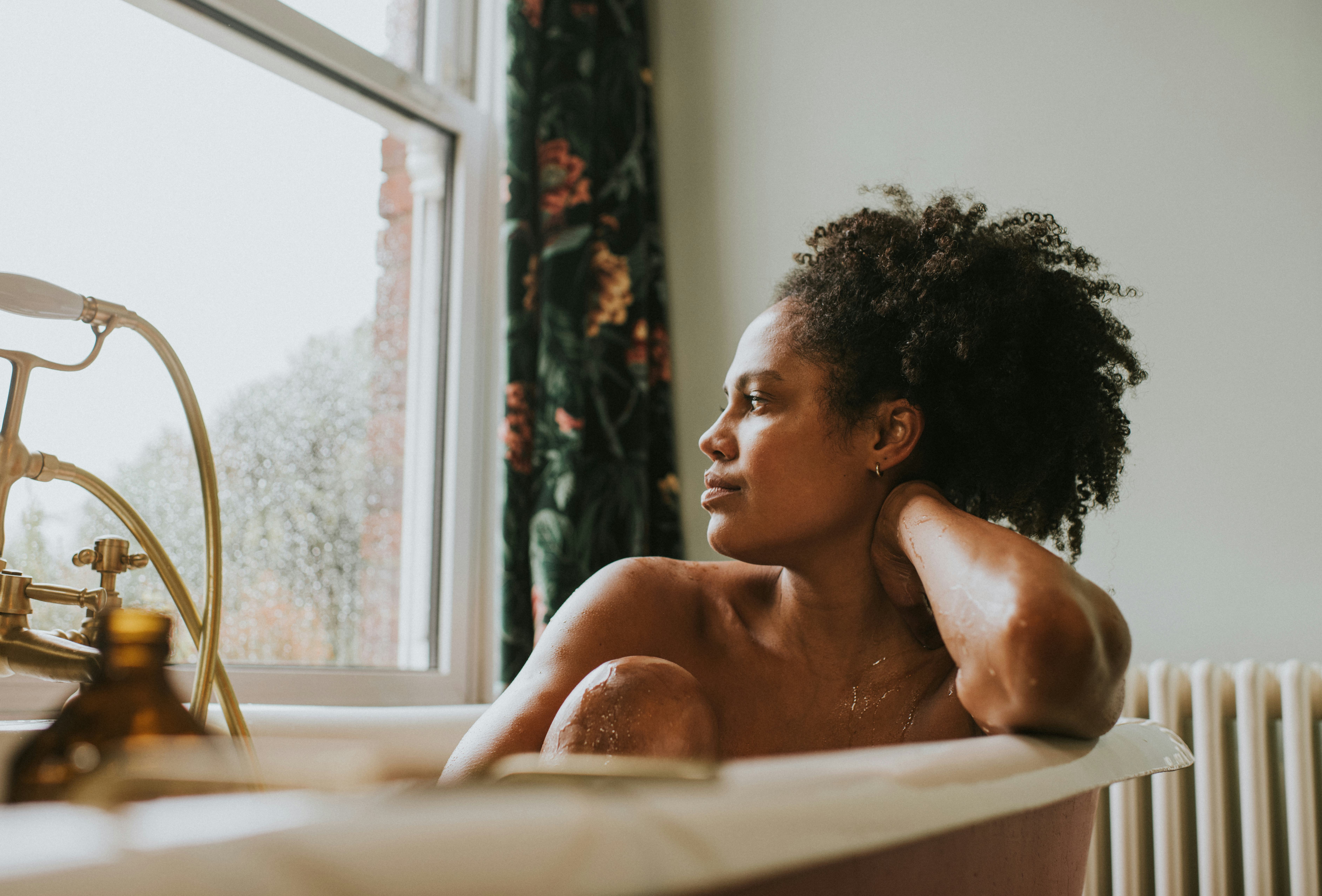 A beautiful woman bathes in a roll top bath. She seems distracted as she rests her head on her arm a...